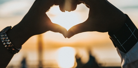 Hands shaped as a heart with a sunset in the background