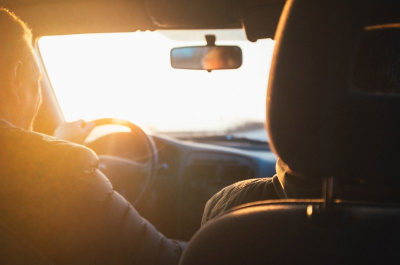 Two people driving a car into the sunrise